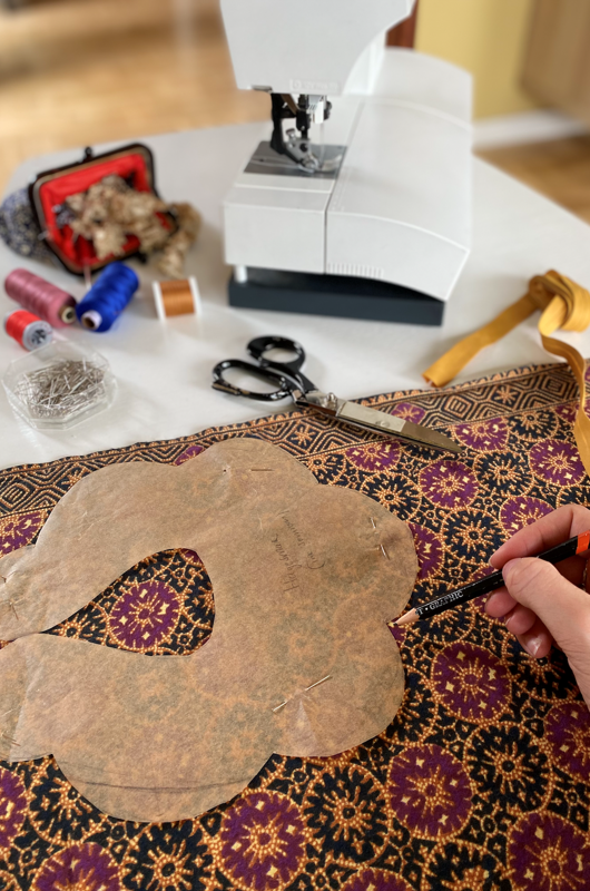 Et arbejdsbord med mønstret stof, konstruktionsmønster, symaskine, blyant, nål, tråd og syredskaber.